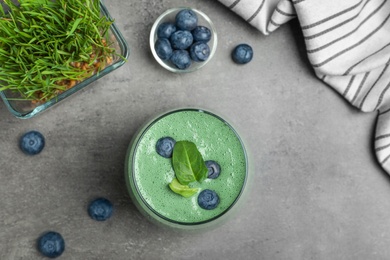 Flat lay composition with spirulina smoothie, wheat grass and blueberries on grey background