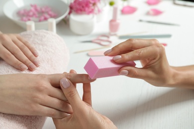 Photo of Manicurist polishing client's nails with buffer at table, closeup. Spa treatment