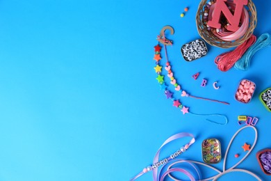 Photo of Kid`s handmade jewelry kit. Colorful beads, ribbon and bracelets on light blue background, flat lay. Space for text