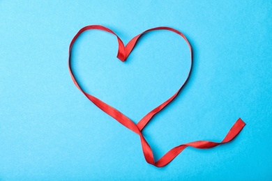 Photo of Heart made of red ribbon on color background, top view