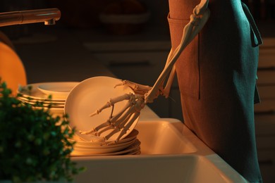 Photo of Human skeleton washing dishes in kitchen sink at night, closeup