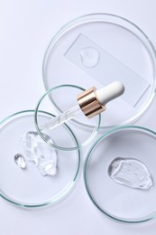 Photo of Petri dishes with samples of cosmetic serums and pipette on white background, flat lay