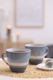 Photo of Cups of drink and snap infuser with dry leaves on table indoors, space for text