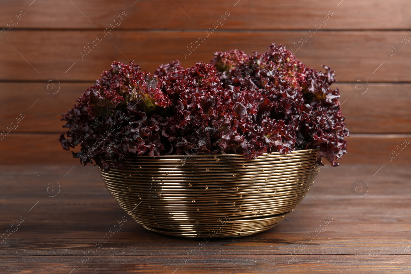 Photo of Bowl with fresh red coral lettuce on wooden table