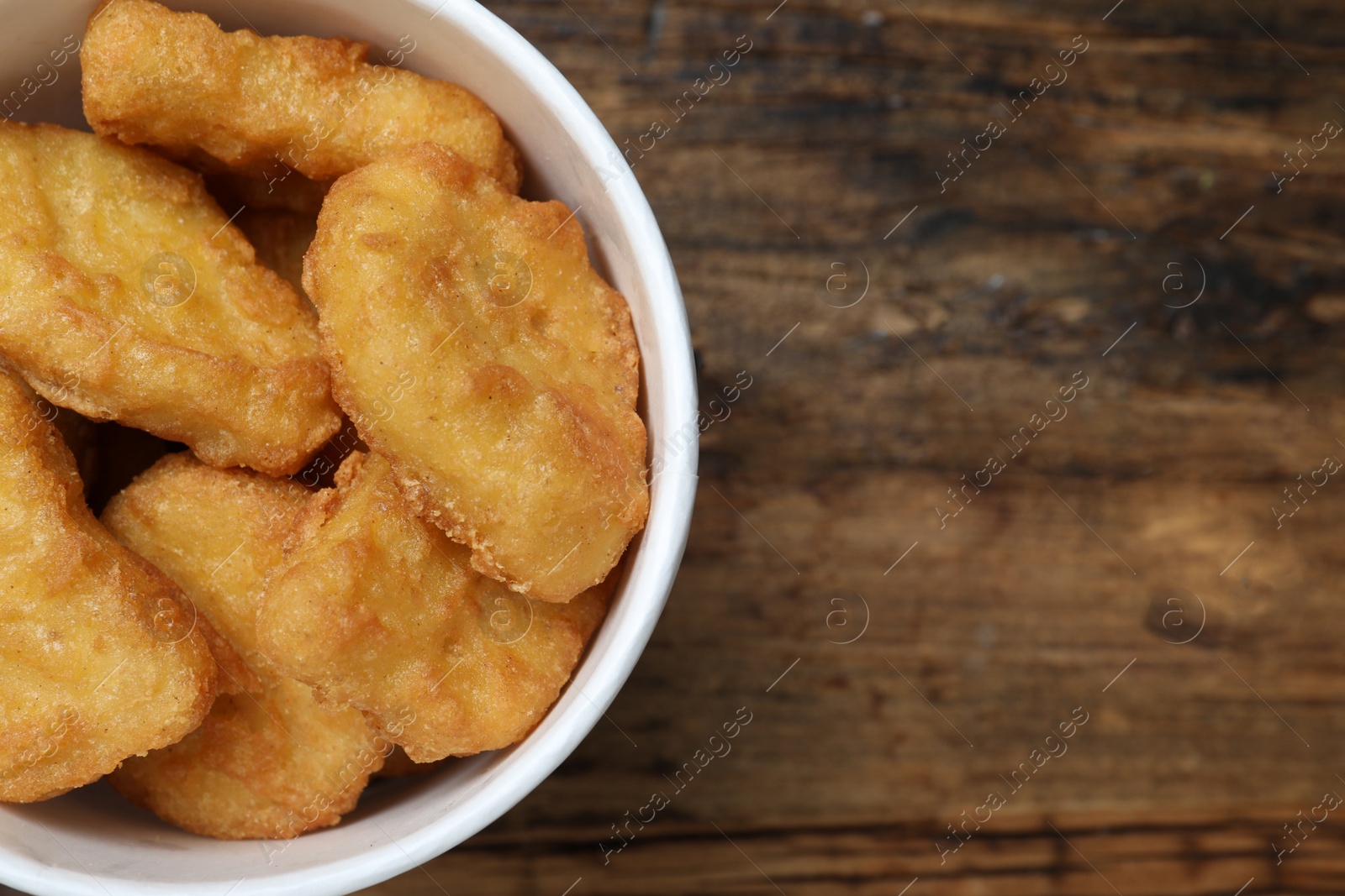 Photo of Bucket with tasty chicken nuggets on wooden table, top view. Space for text