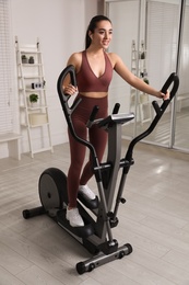 Happy young woman training on elliptical machine at home