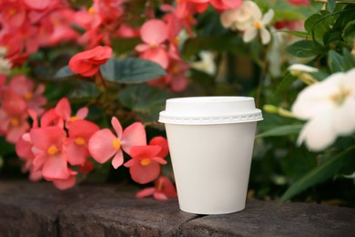 Cardboard cup with tasty coffee near beautiful flowers outdoors. Space for text