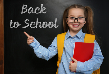 Cute little child wearing glasses near chalkboard with phrase BACK TO SCHOOL