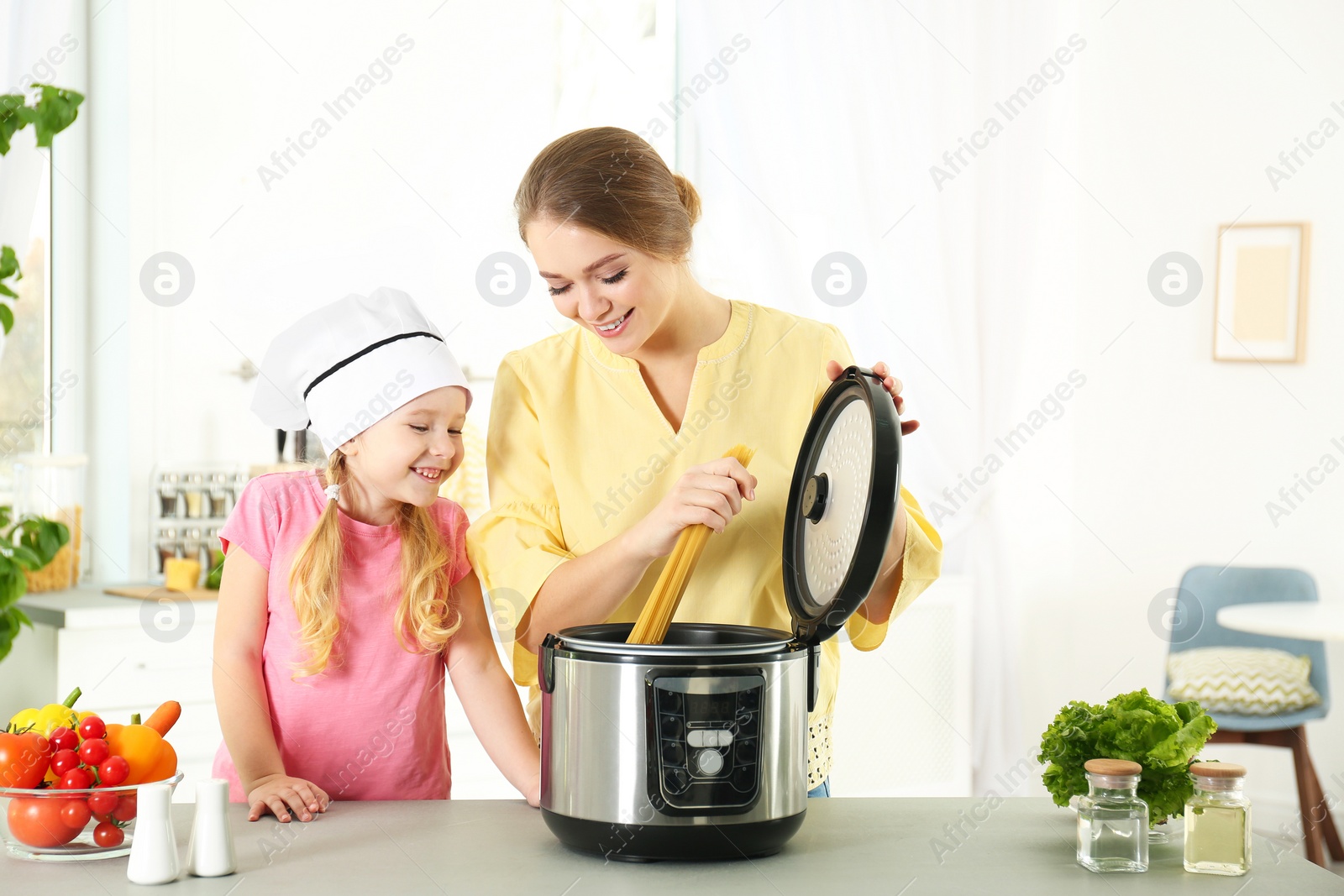 Photo of Mother and daughter preparing food with modern multi cooker in kitchen