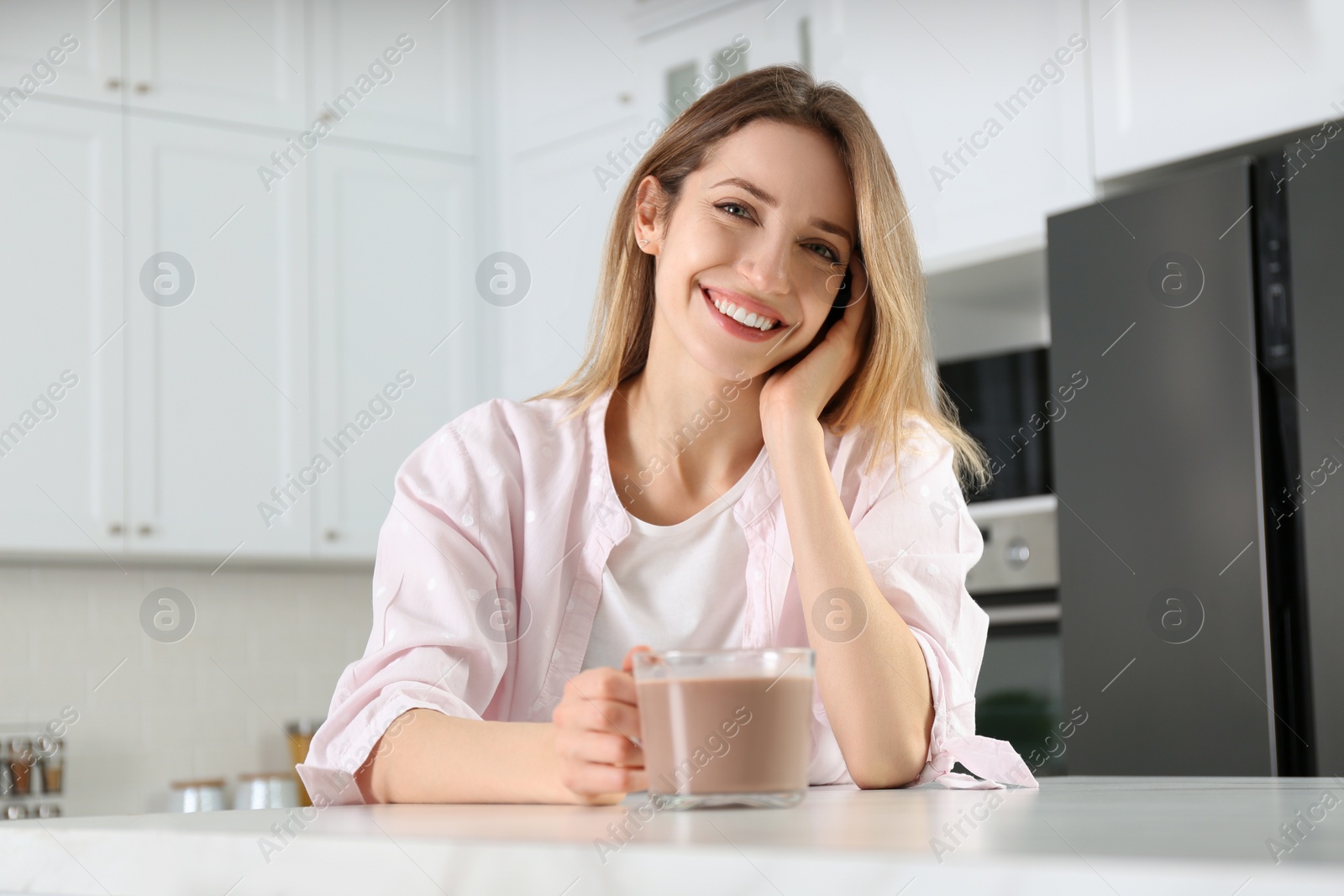 Photo of Young woman with glass cup of chocolate milk in kitchen