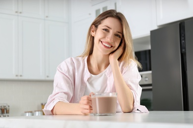 Young woman with glass cup of chocolate milk in kitchen