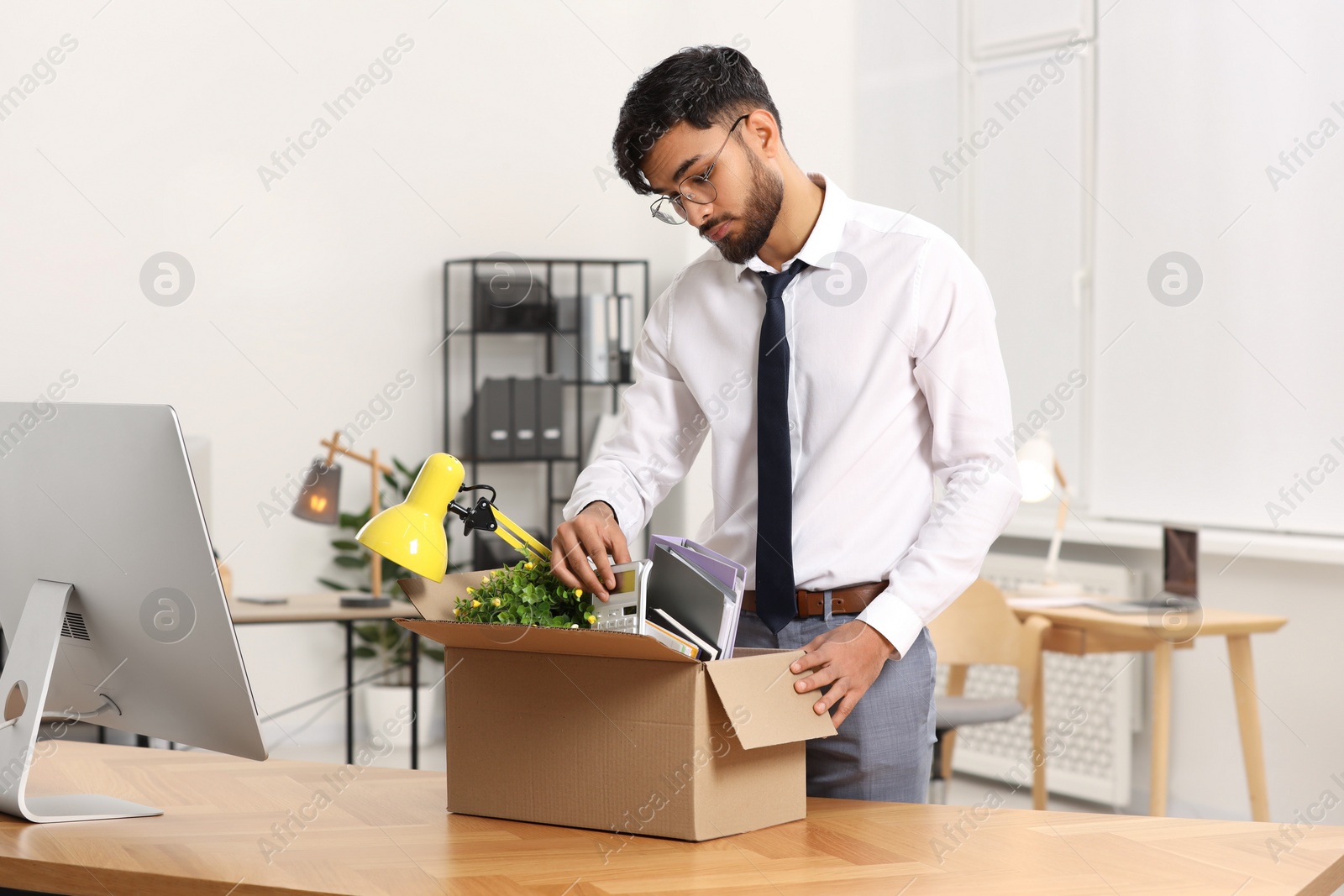 Photo of Unemployment problem. Frustrated man with box of personal belongings at table in office