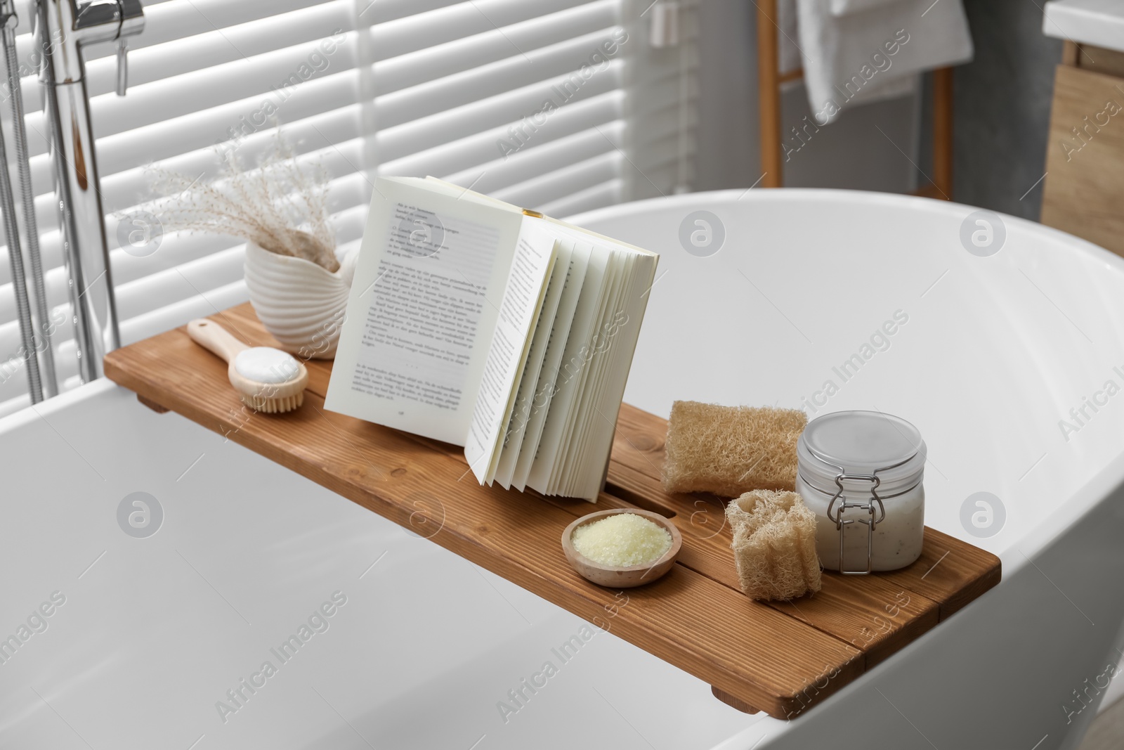 Photo of Wooden tray with spa products and book on bath tub in bathroom