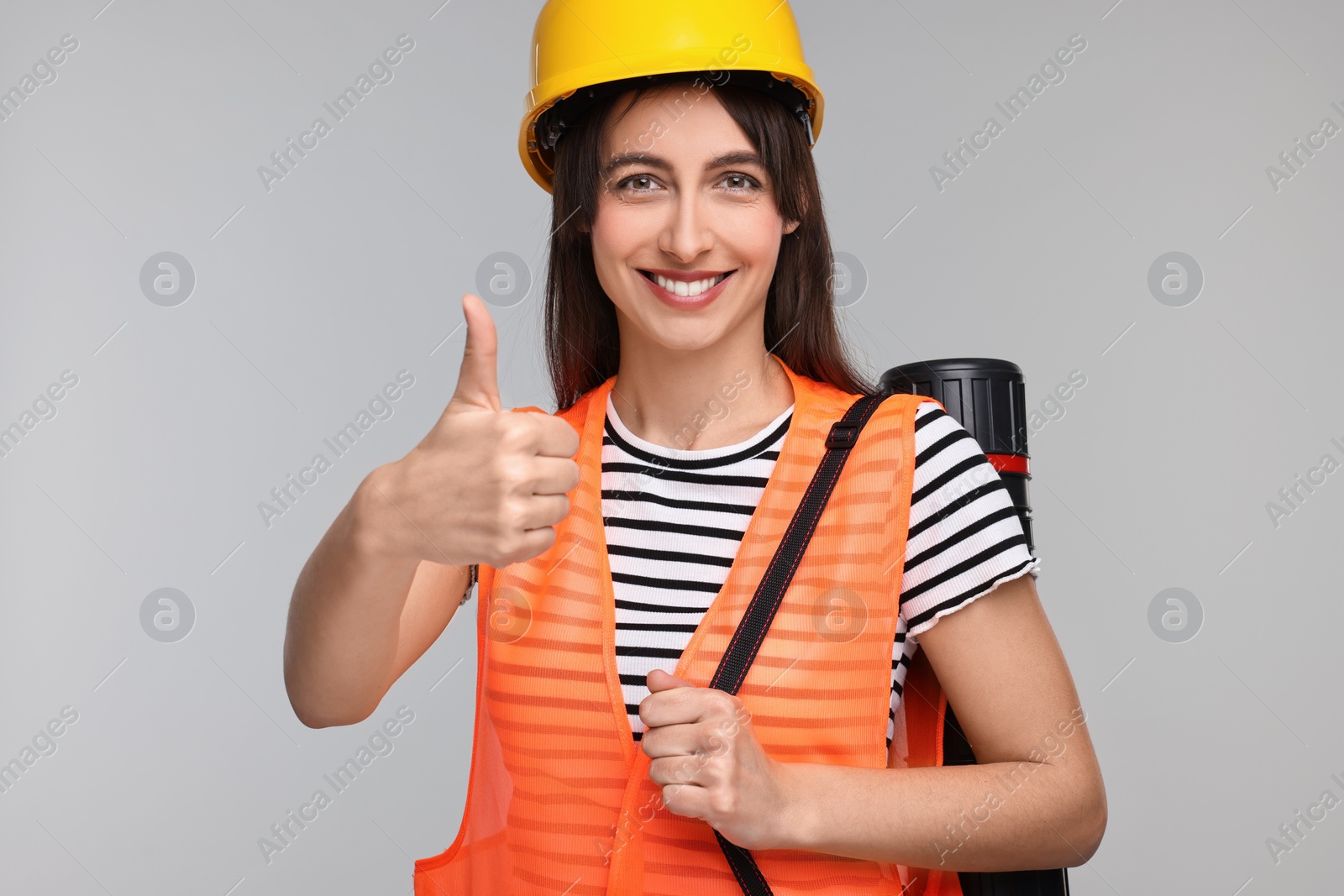 Photo of Architect in hard hat with tube showing thumbs up on light grey background