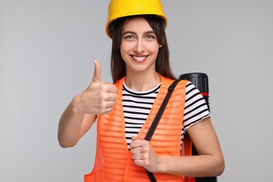 Architect in hard hat with tube showing thumbs up on light grey background