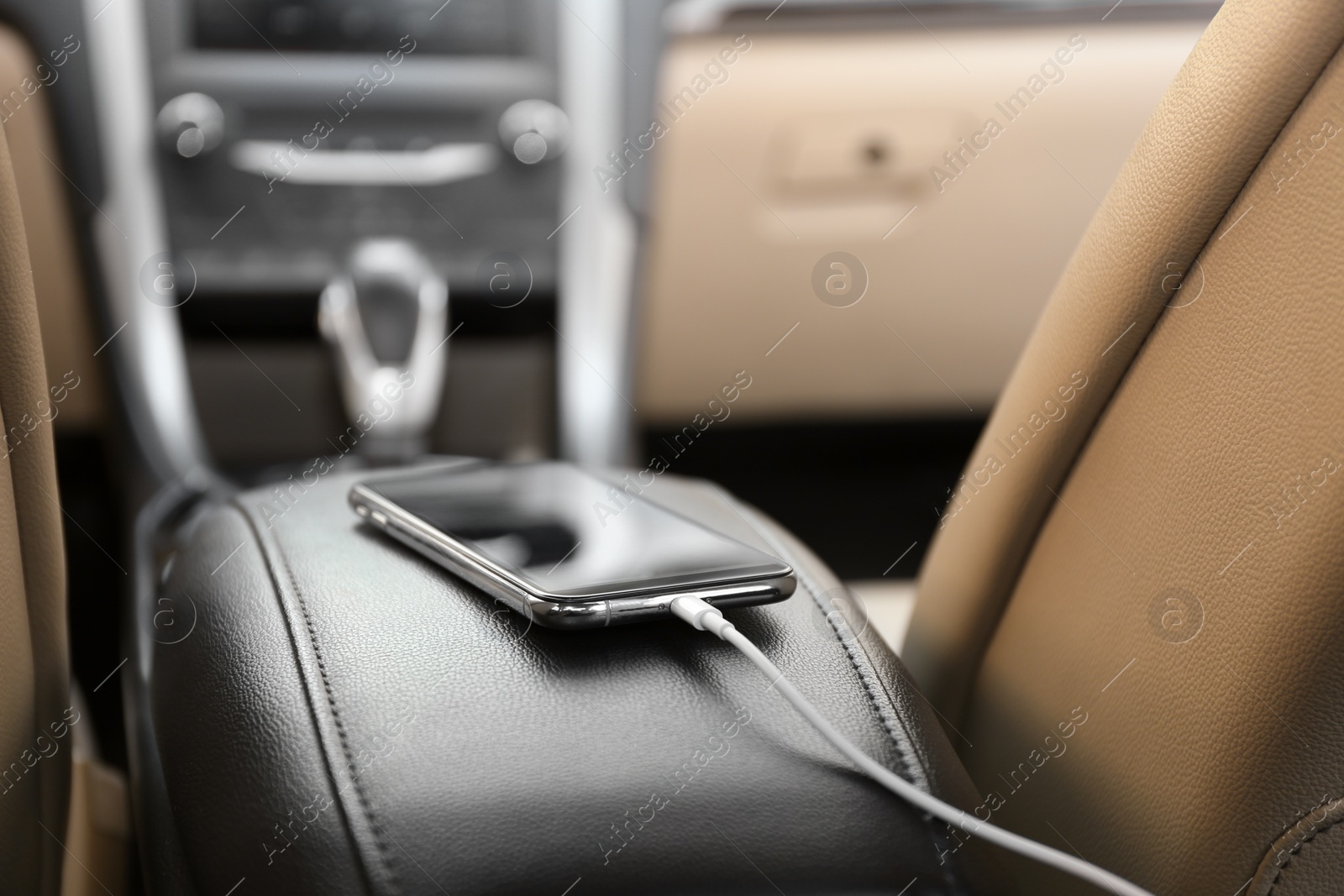 Photo of Mobile phone with charging cable in car, closeup