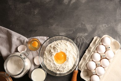Photo of Making dough. Flour with egg yolk in bowl and other products on grey textured table, flat lay