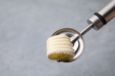 Photo of Tasty butter curl in spoon on light grey table, closeup. Space for text