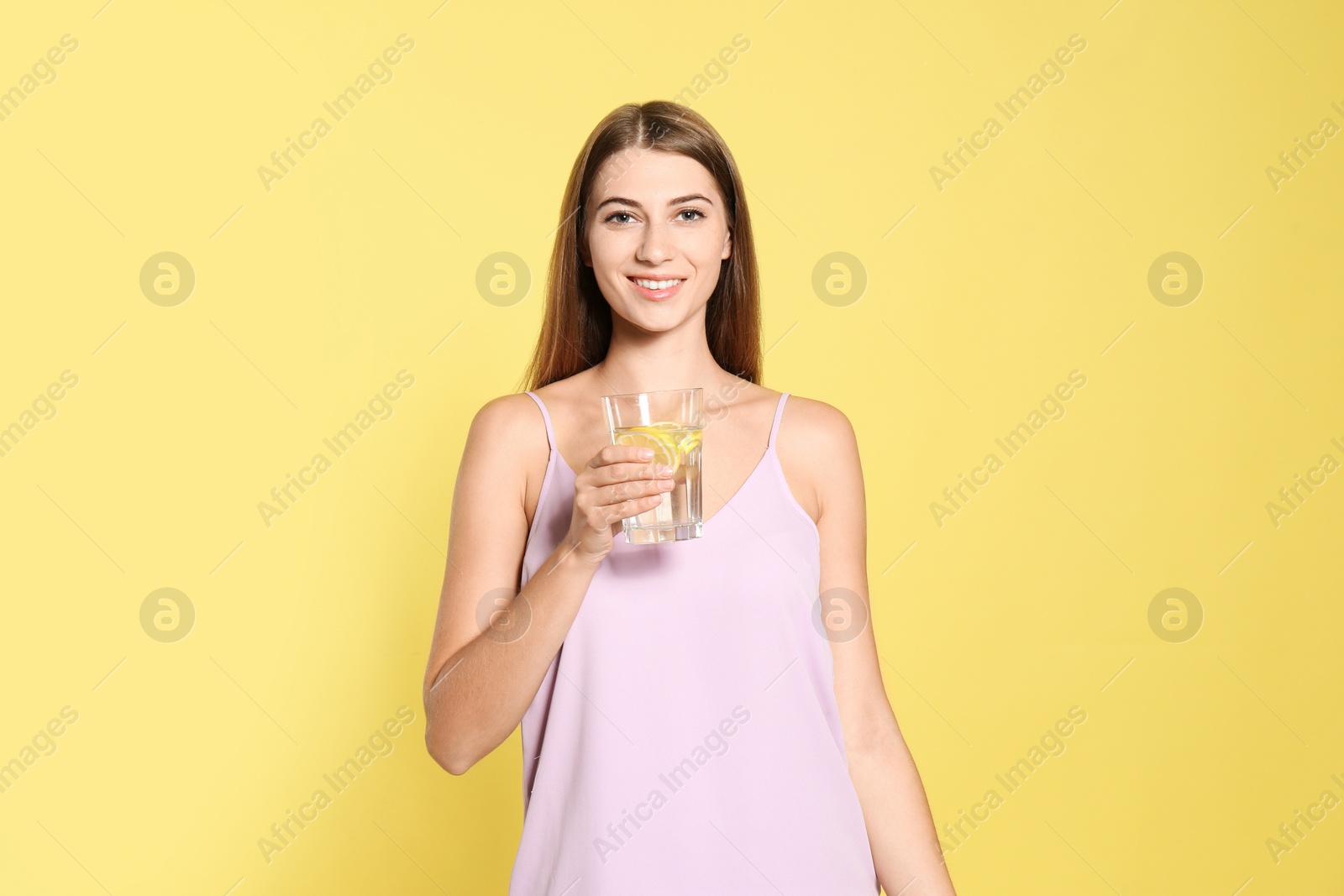 Photo of Young woman with glass of lemon water on yellow background