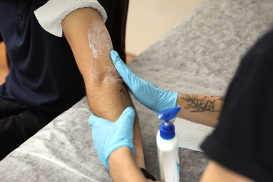 Photo of Professional tattoo master working with client in salon, closeup