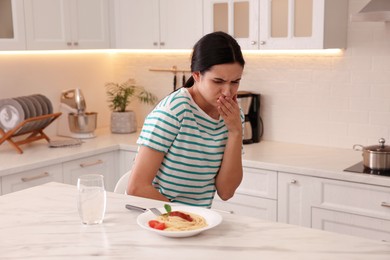 Photo of Young woman feeling nausea while seeing food at table in kitchen