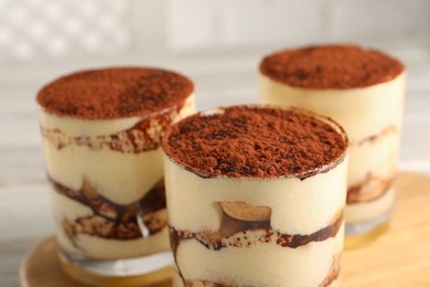 Photo of Delicious tiramisu in glasses on blurred background, closeup