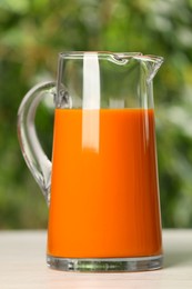 Photo of Tasty carrot juice on white table outdoors, closeup