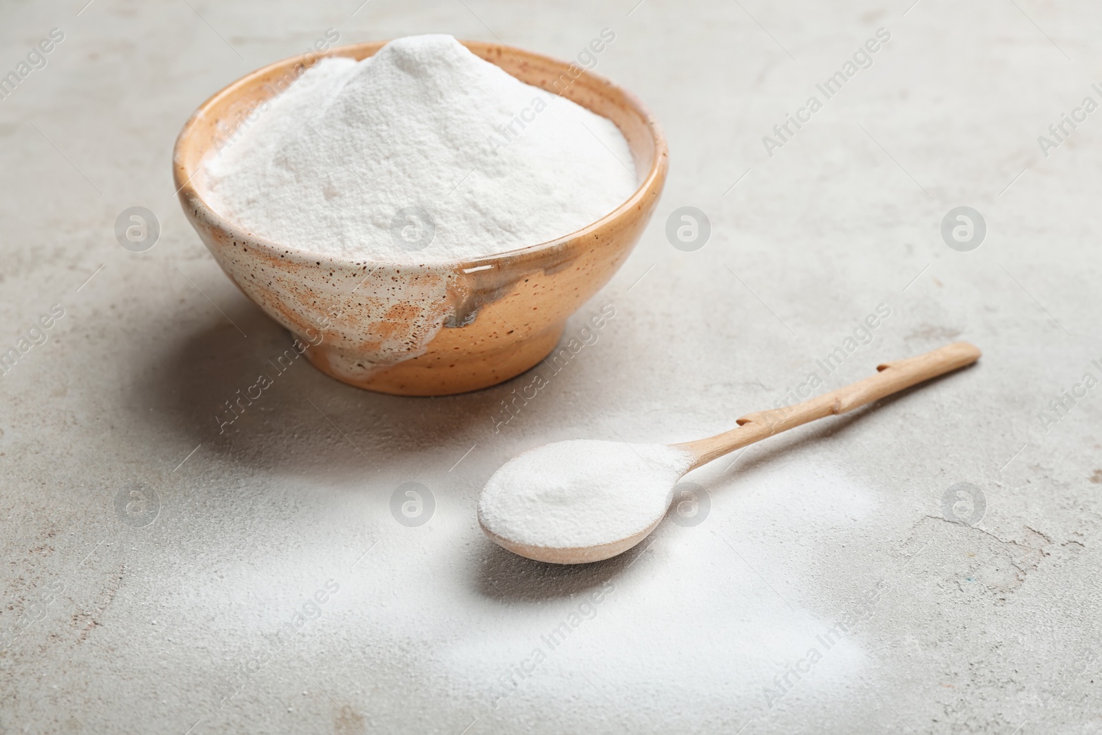 Photo of Spoon and bowl with baking soda on grey background