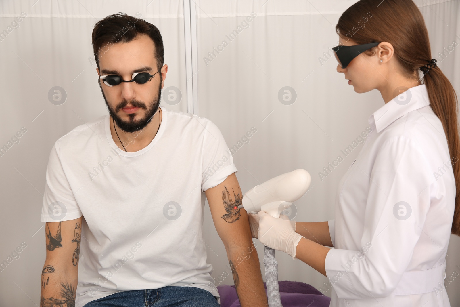 Photo of Young man undergoing laser tattoo removal procedure in salon