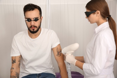 Photo of Young man undergoing laser tattoo removal procedure in salon