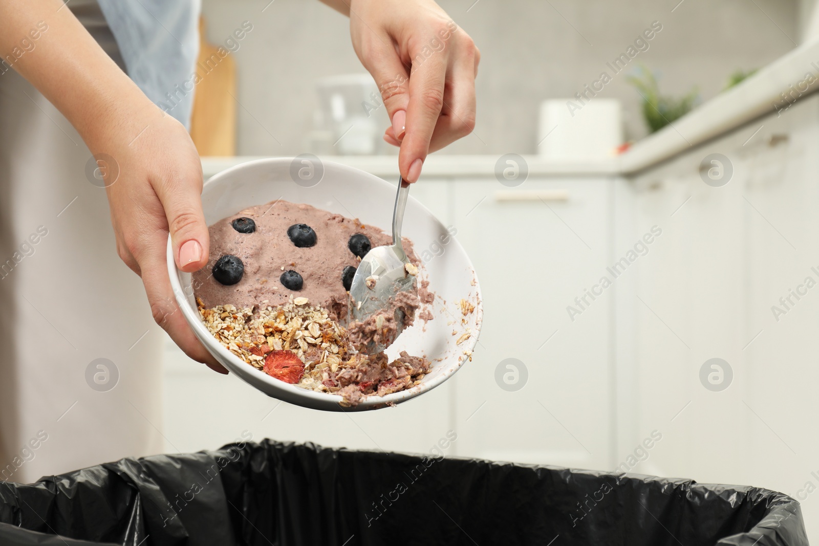 Photo of Woman throwing oatmeal with berries into bin indoors, closeup