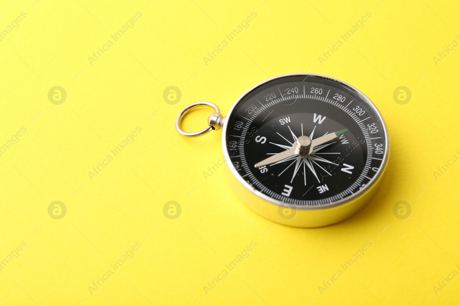 Photo of One compass on yellow background, space for text. Tourist equipment