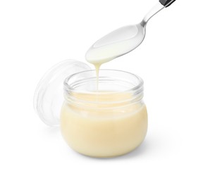 Photo of Condensed milk flowing down from spoon into jar isolated on white