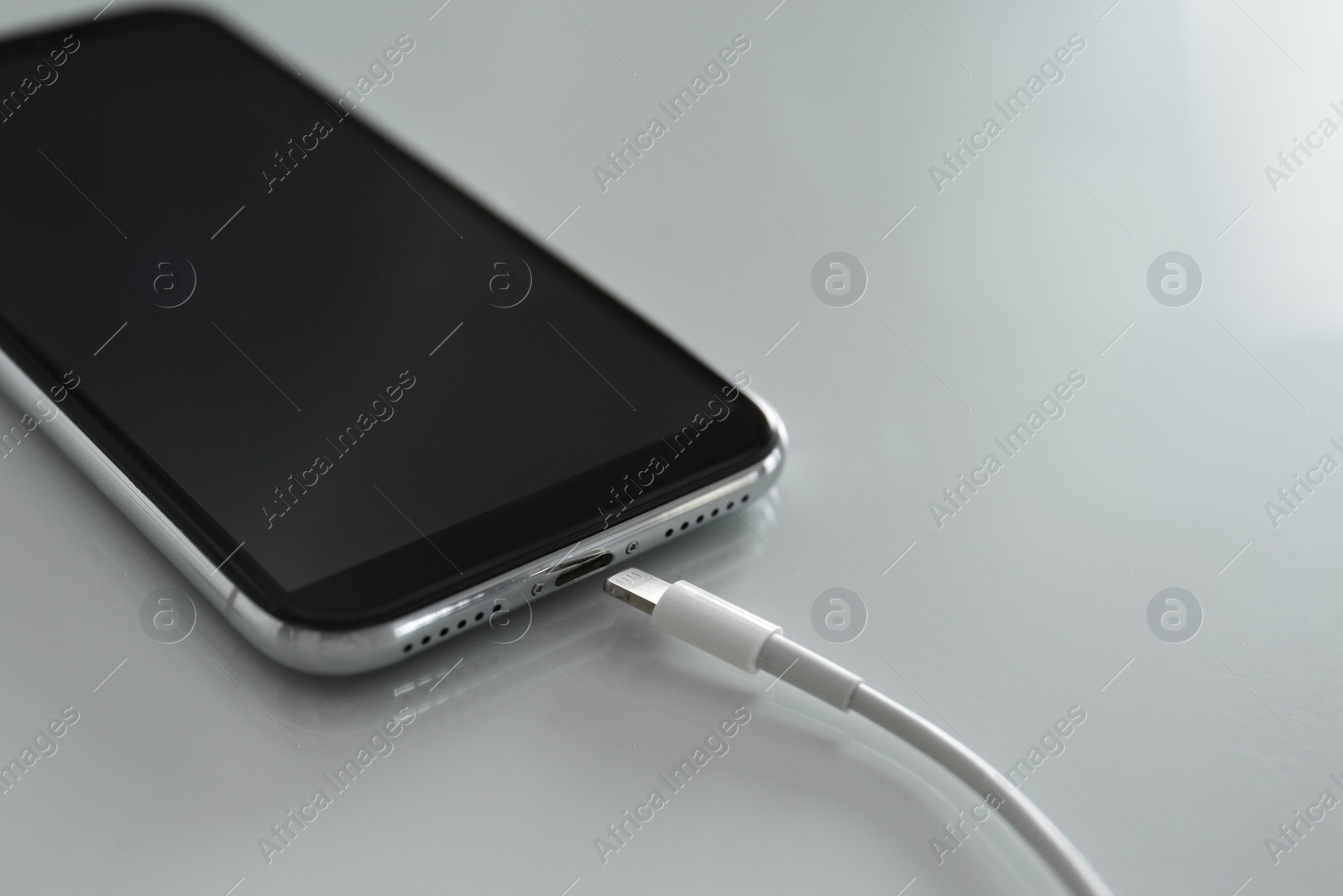 Photo of Mobile phone and charging cable on white table, closeup