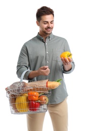 Photo of Young man with bell pepper and shopping basket full of products isolated on white