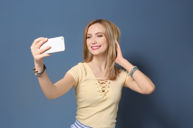 Photo of Attractive young woman taking selfie on color background