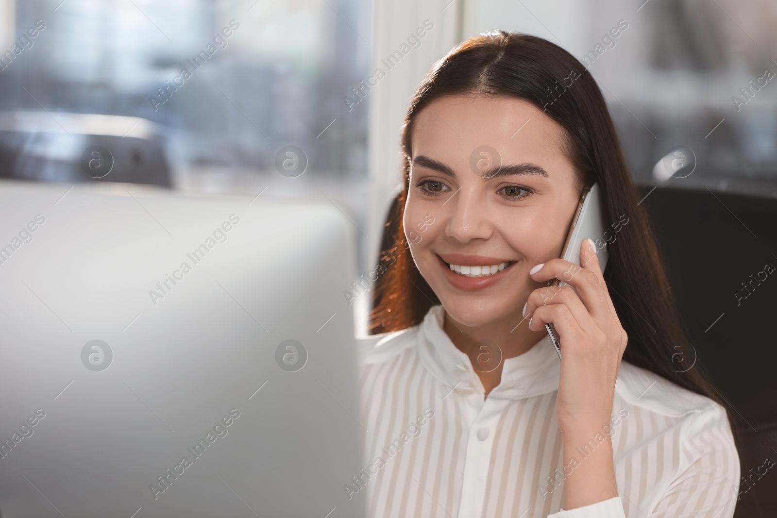 Photo of Happy woman using modern computer while talking on smartphone in office