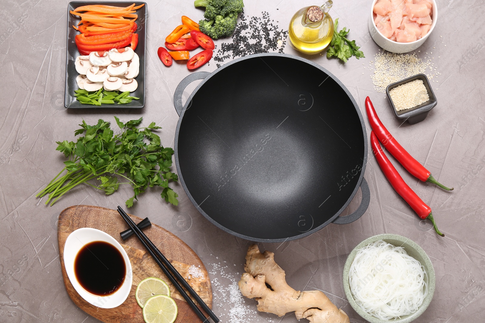 Photo of Wok, chopsticks and different products on grey textured table, flat lay