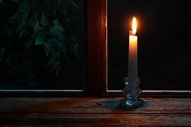 Photo of Burning candle on wooden table near window at night