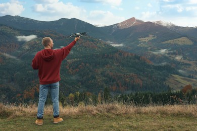 Young man with modern drone in mountains, back view. Space for text
