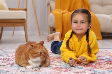 Photo of Little girl and cute ginger cat on carpet at home