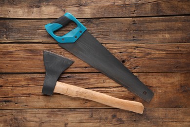 Saw with light blue handle and axe on wooden background, flat lay