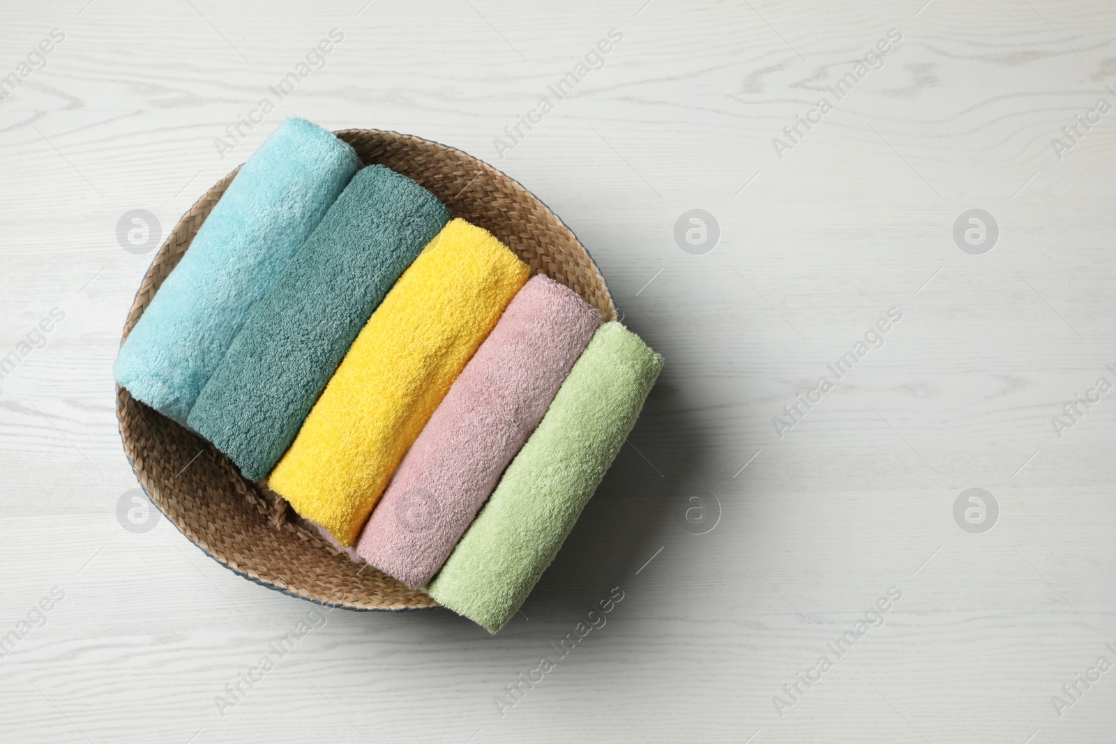 Photo of Wicker basket with folded towels on white wooden surface, top view. Space for text