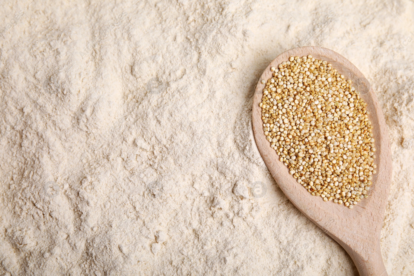 Photo of Spoon with quinoa seeds on flour, top view. Space for text