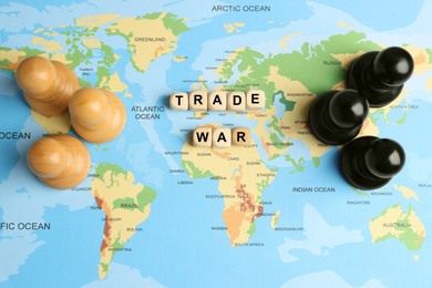 Photo of Wooden cubes with phrase Trade war and chess pieces on world map, flat lay