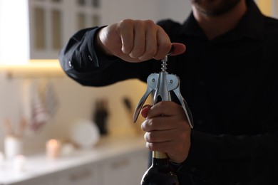 Man opening wine bottle with corkscrew indoors, closeup