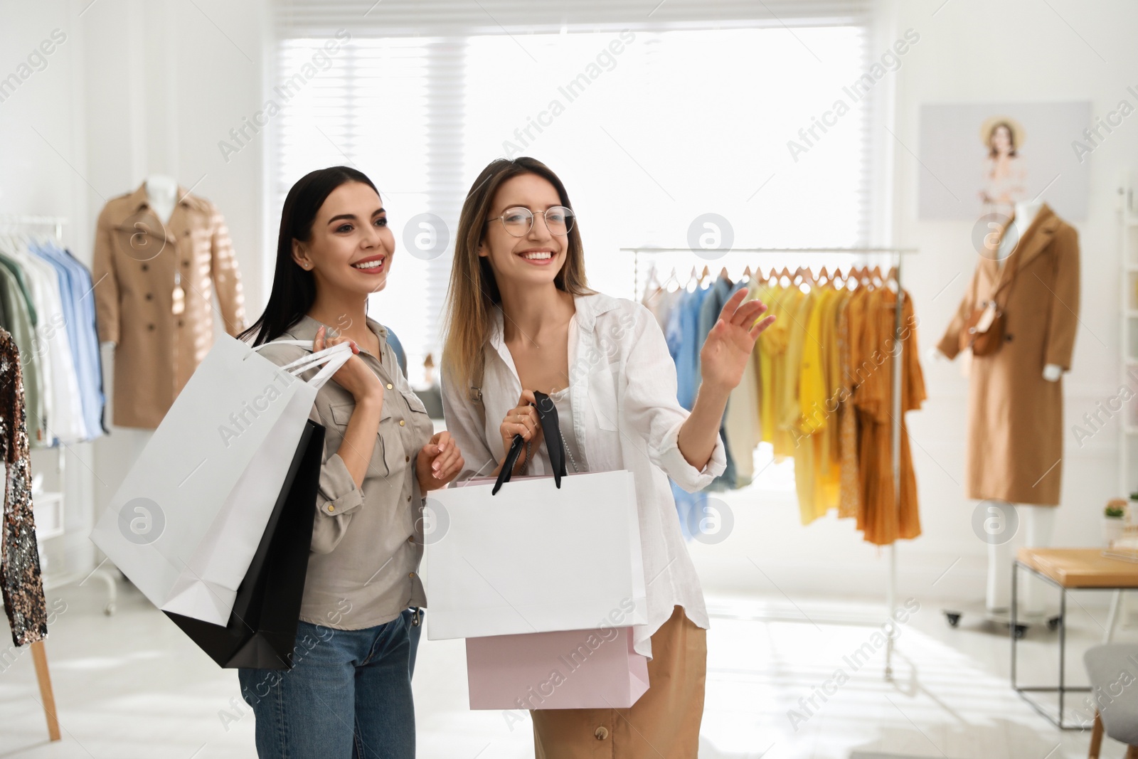 Photo of Young women with shopping bags choosing clothes in modern boutique