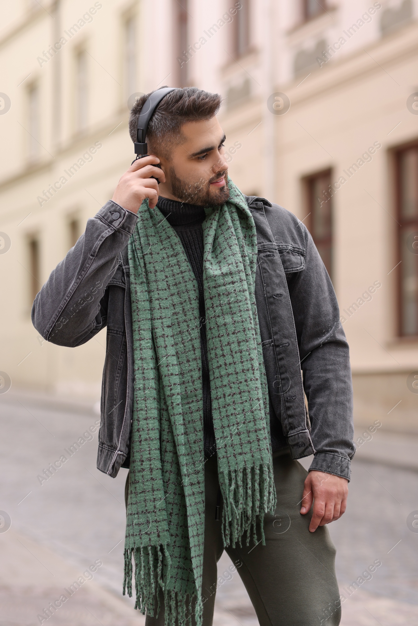 Photo of Handsome man in warm scarf listening to music outdoors