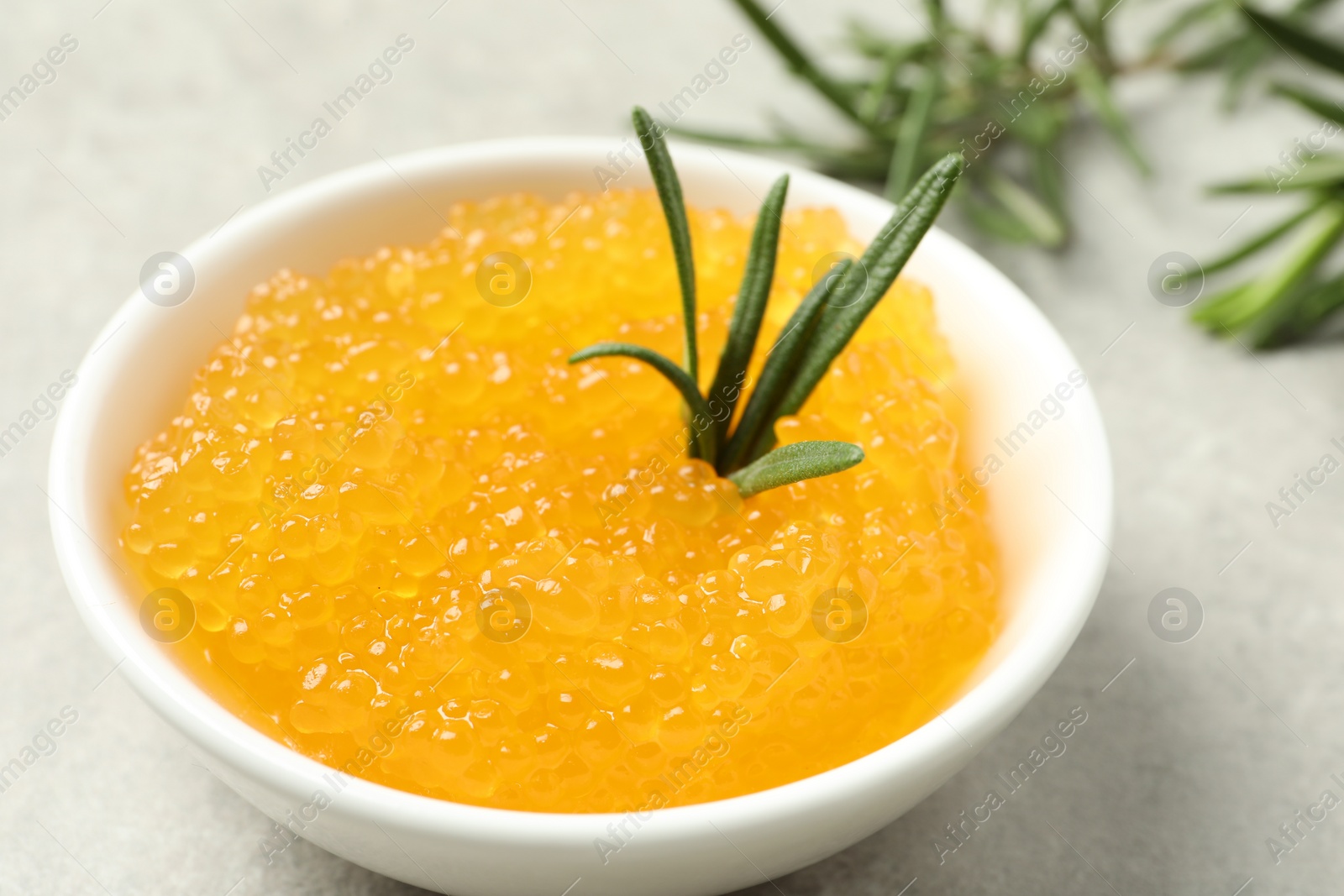 Photo of Fresh pike caviar in bowl and rosemary on light grey table, closeup