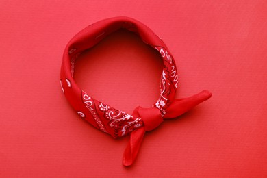Tied bandana with paisley pattern on red background, top view
